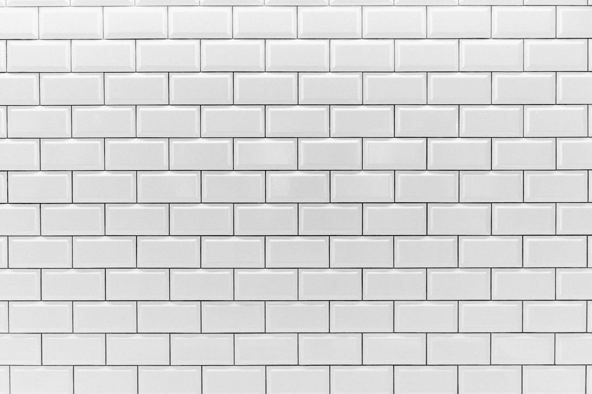 Un mur entièrement recouvert de carreaux blancs rectangulaires à bords biseautés, posés en quinconce et séparés par de fins joints sombres.